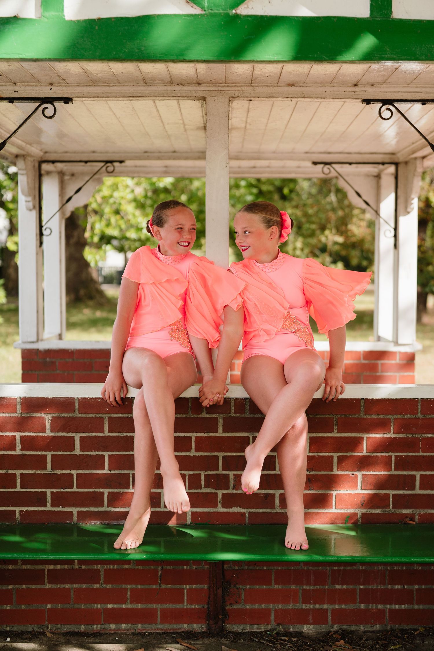 Two matching coral outfits photographed in sequence on a covered porch with brick details. Manningtree, Essex.