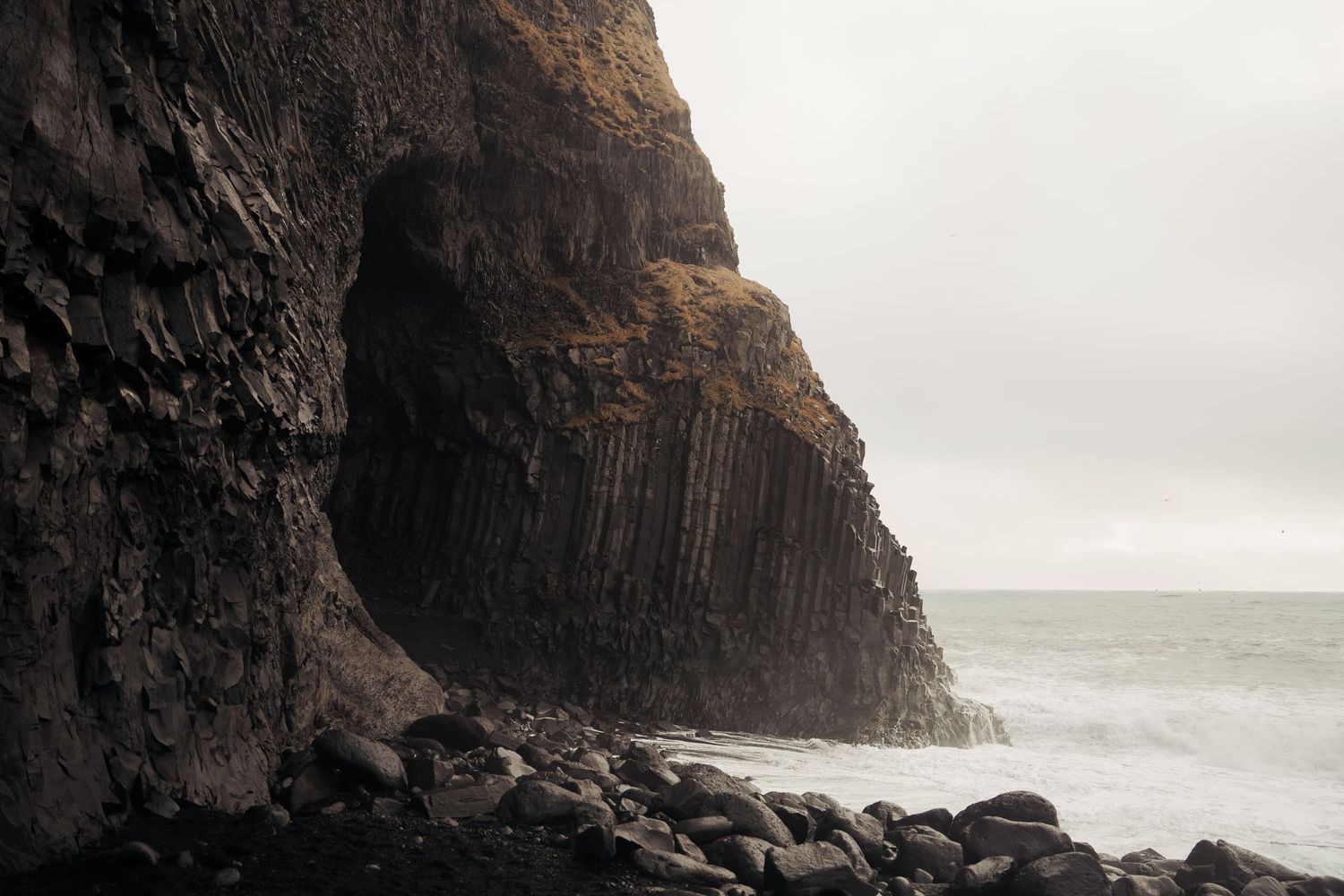 Basalt columns and rocky cliffs tower over a rugged black sand beach with crashing waves. Iceland.
