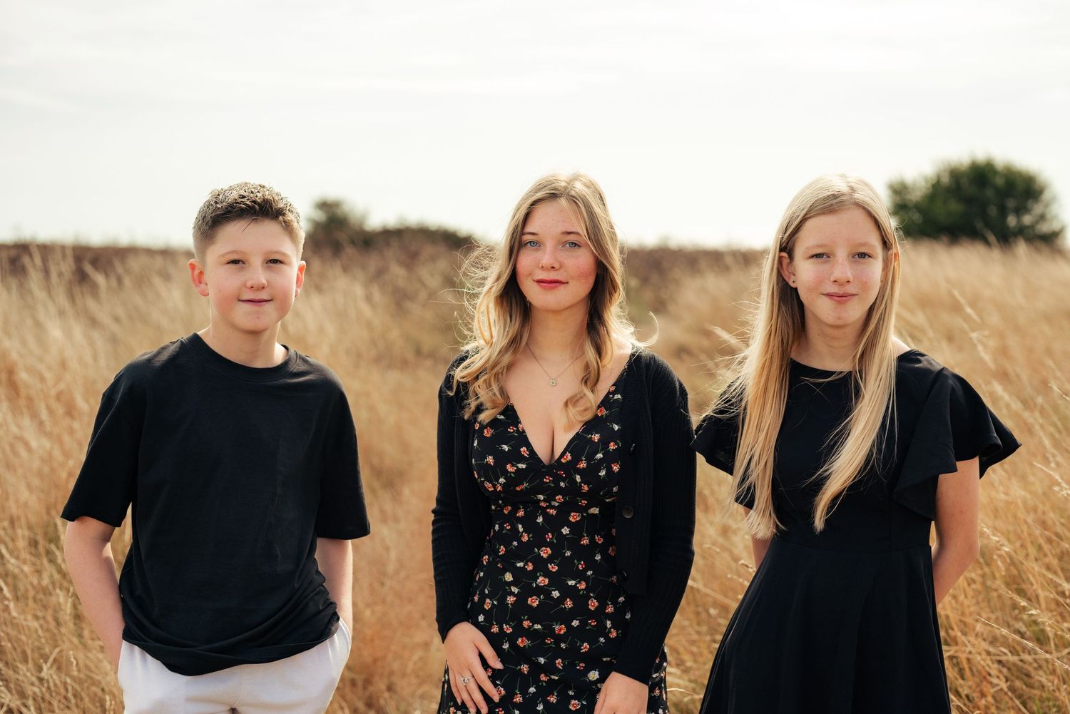 Family members pose together in coordinated black outfits against a sunny field backdrop. Earlhams Beach, Harwich, Essex.
