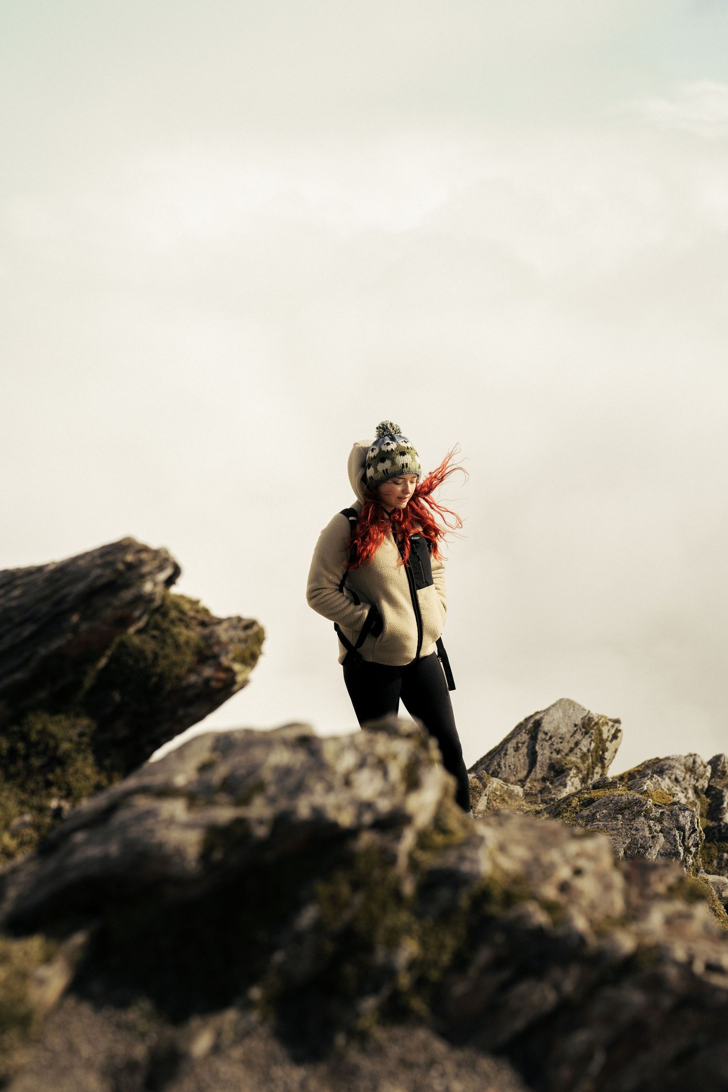 A hiker stands on rocky terrain against an overcast sky wearing winter gear. Wales.