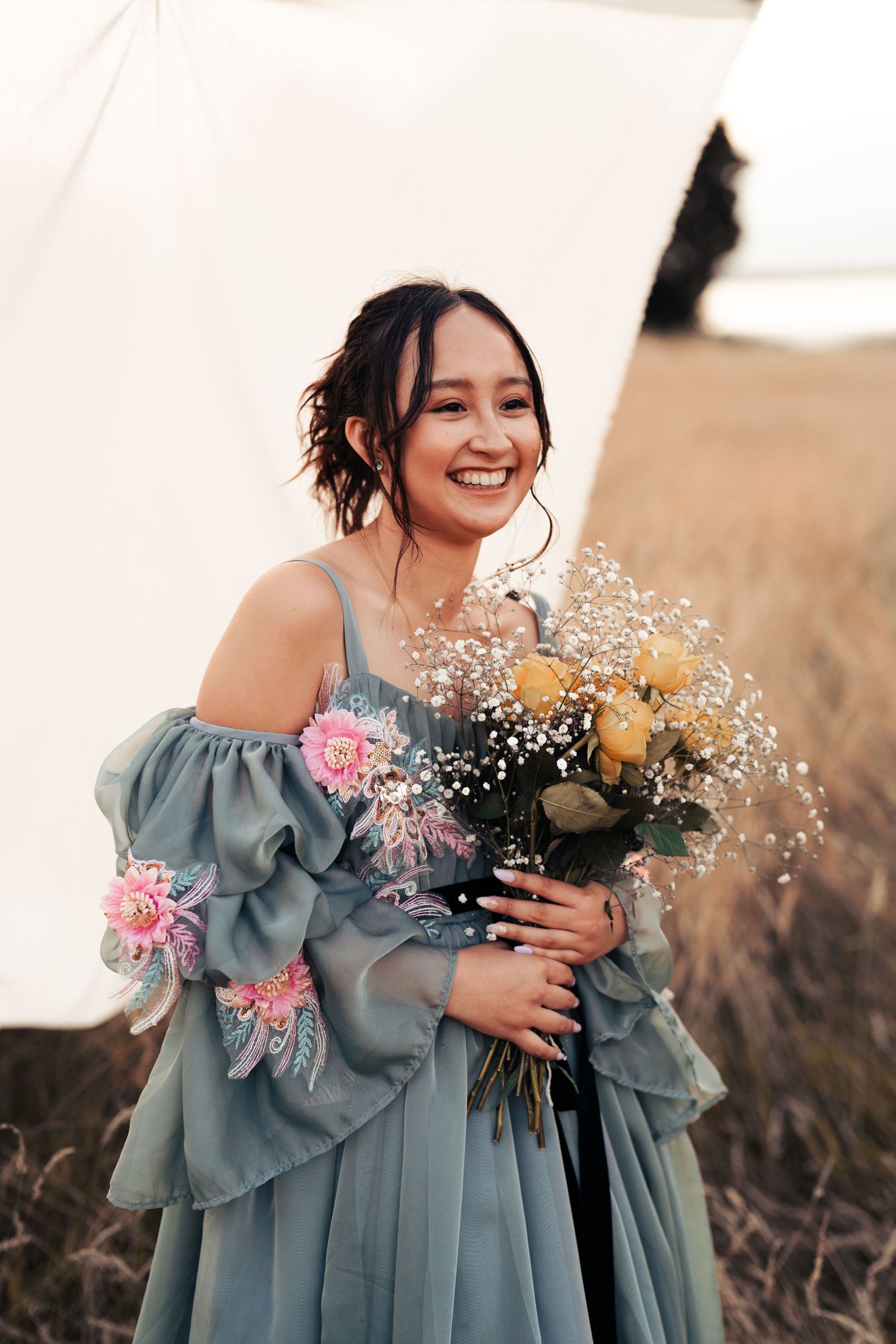 Person in blue ruffled dress holding delicate flowers while laughing in golden sunlight. Wrabness, Essex.