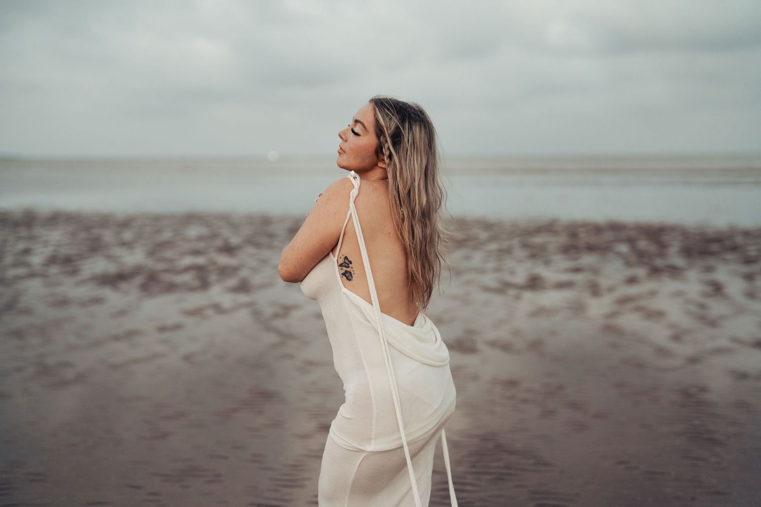 Elegant beach photography series featuring flowing white dress against cloudy sky. Earlhams Beach, Harwich, Essex.