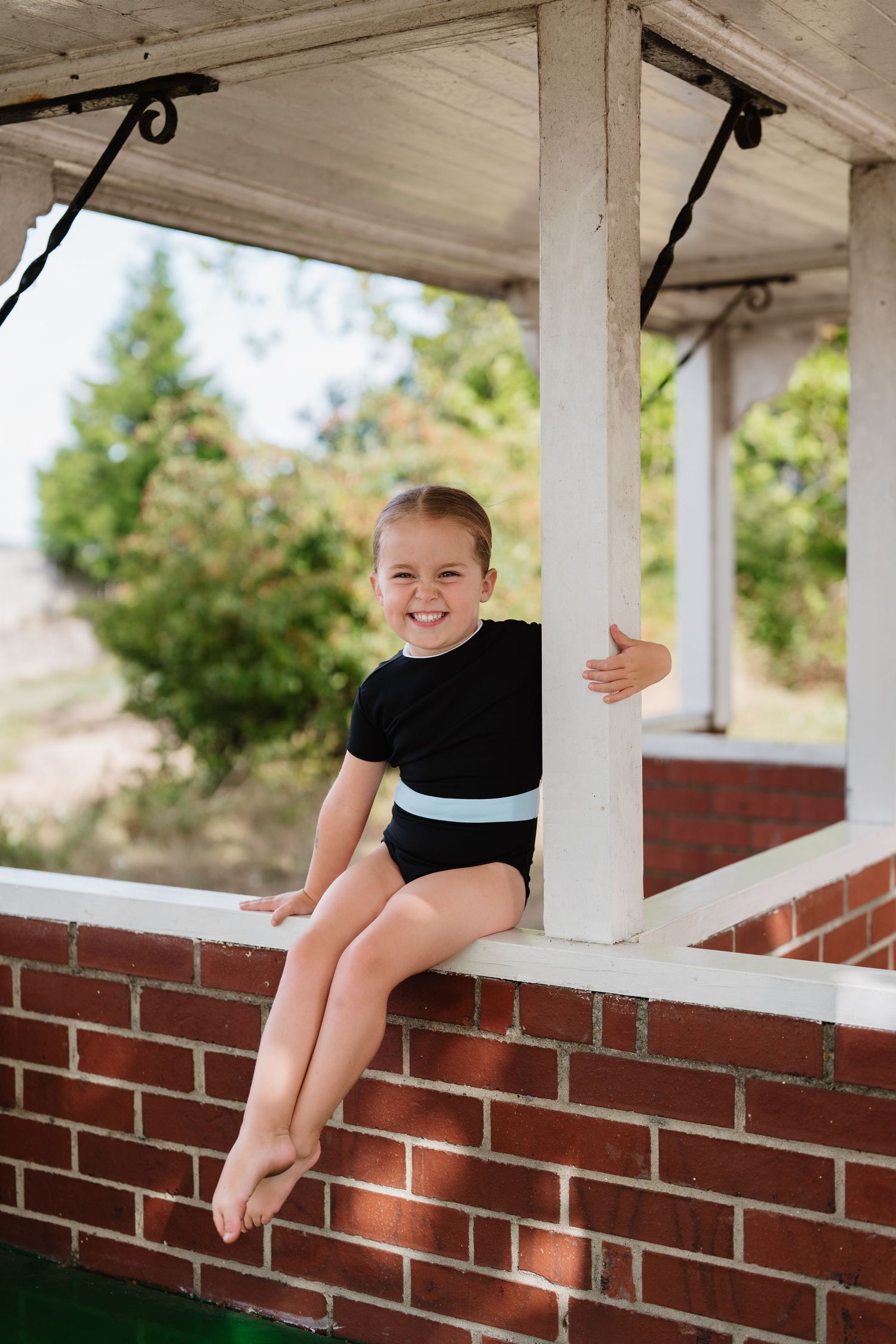 Young athlete sitting on brick ledge of covered porch during outdoor training break. Manningtree, Essex.