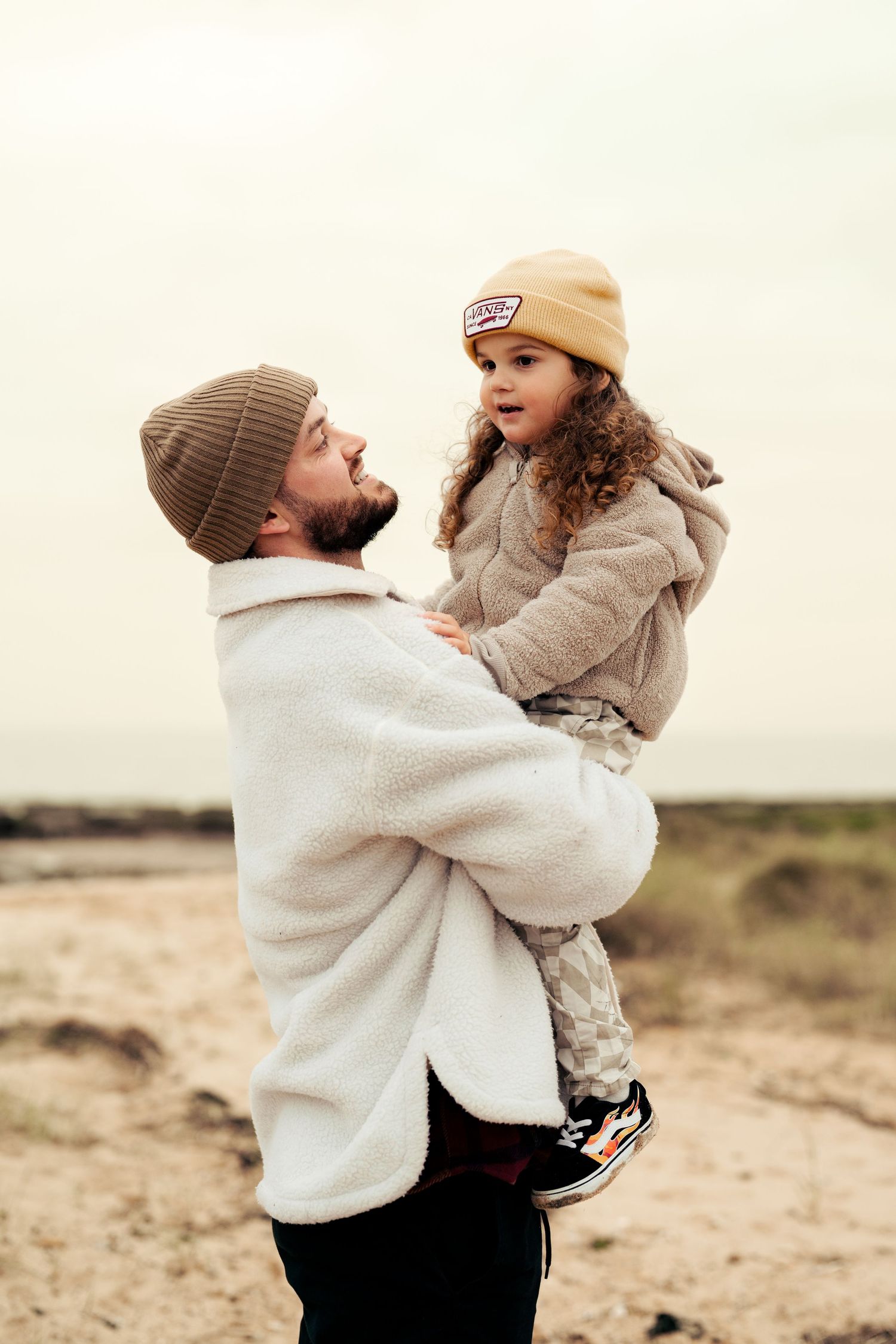 Parent and child sharing playful moment outdoors in warm winter clothing. Earlhams Beach, Harwich, Essex.