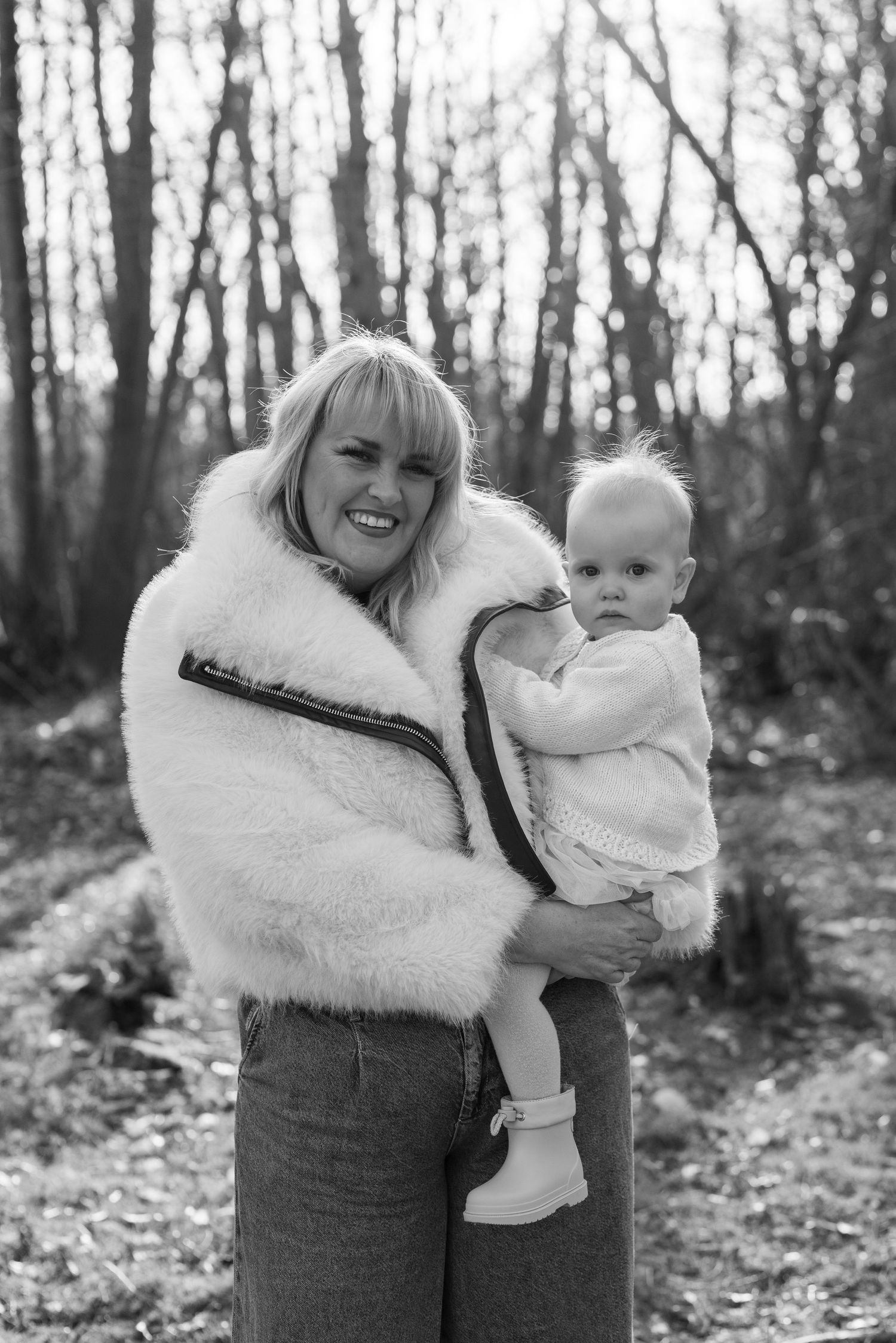 Black and white portraits of parent and baby in a winter forest setting. Wrabness Woods, Essex.
