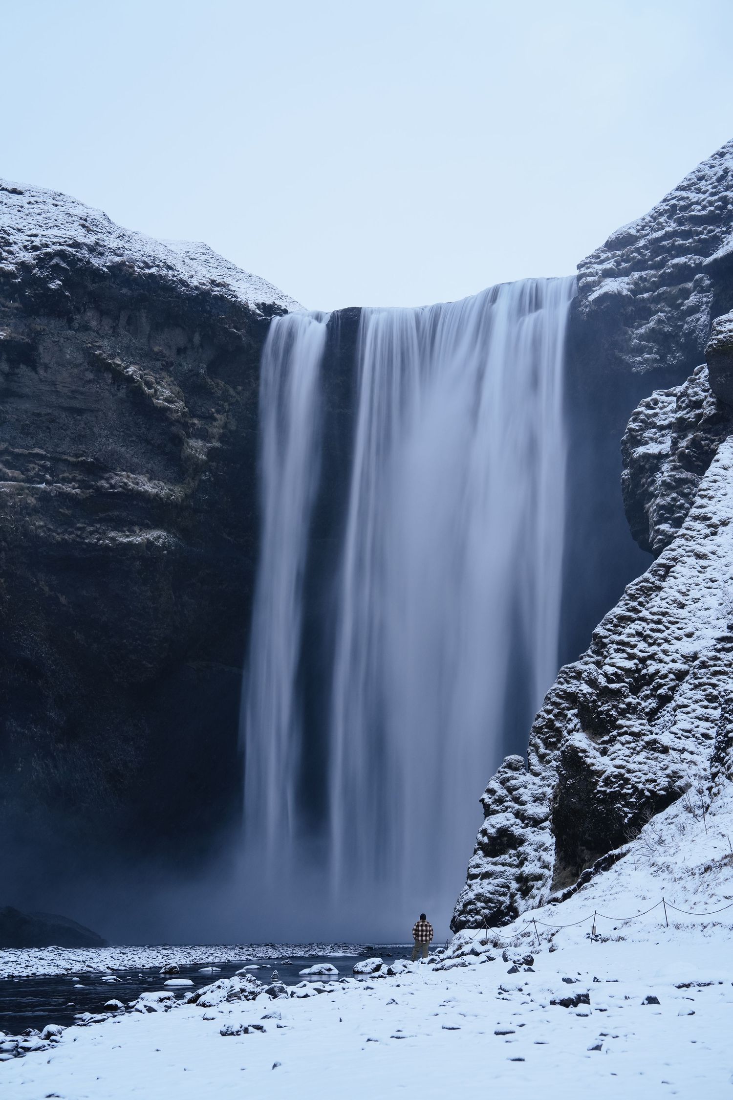 Majestic waterfall cascades down snow-covered cliffs in a winter landscape. Iceland.