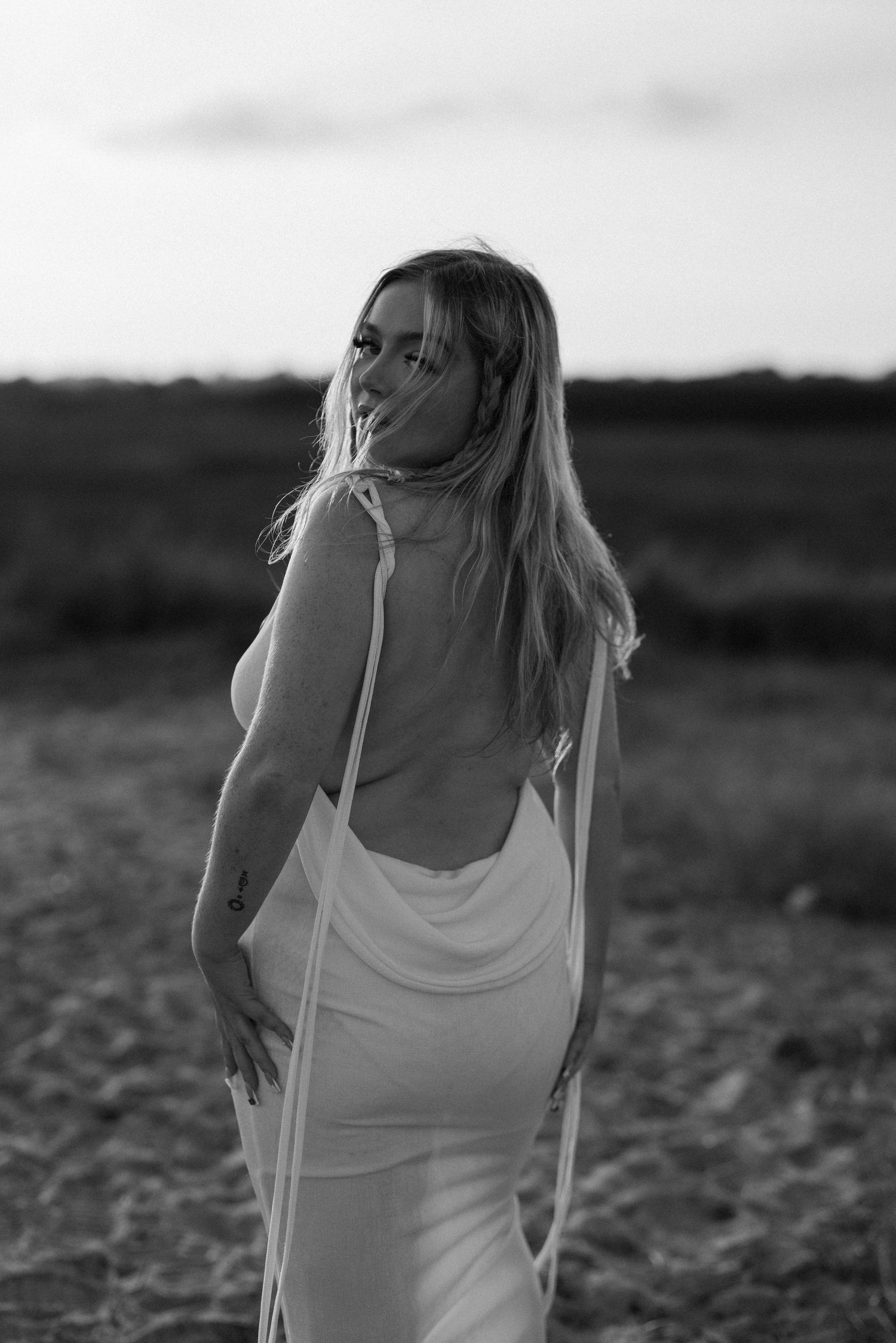 Black and white artistic portrait in flowing dress against rural landscape. Earlhams Beach, Harwich, Essex.