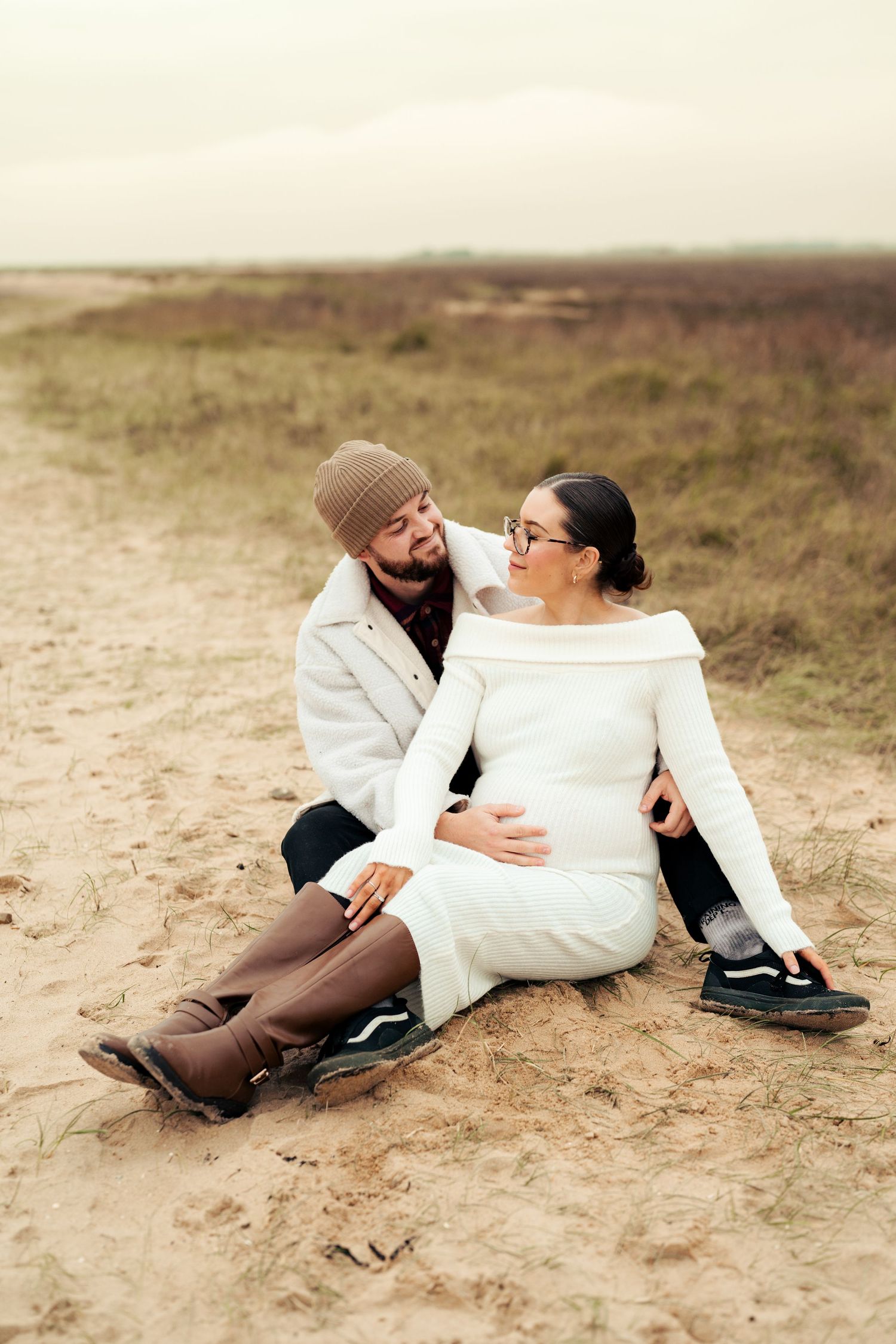 Couple lying on sandy ground in casual winter attire sharing intimate moments at beach. Earlhams Beach, Harwich, Essex.