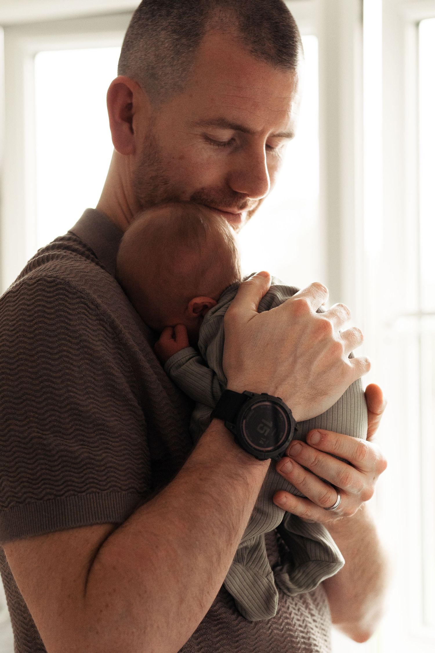 Tender moment between parent and infant in soft window light.