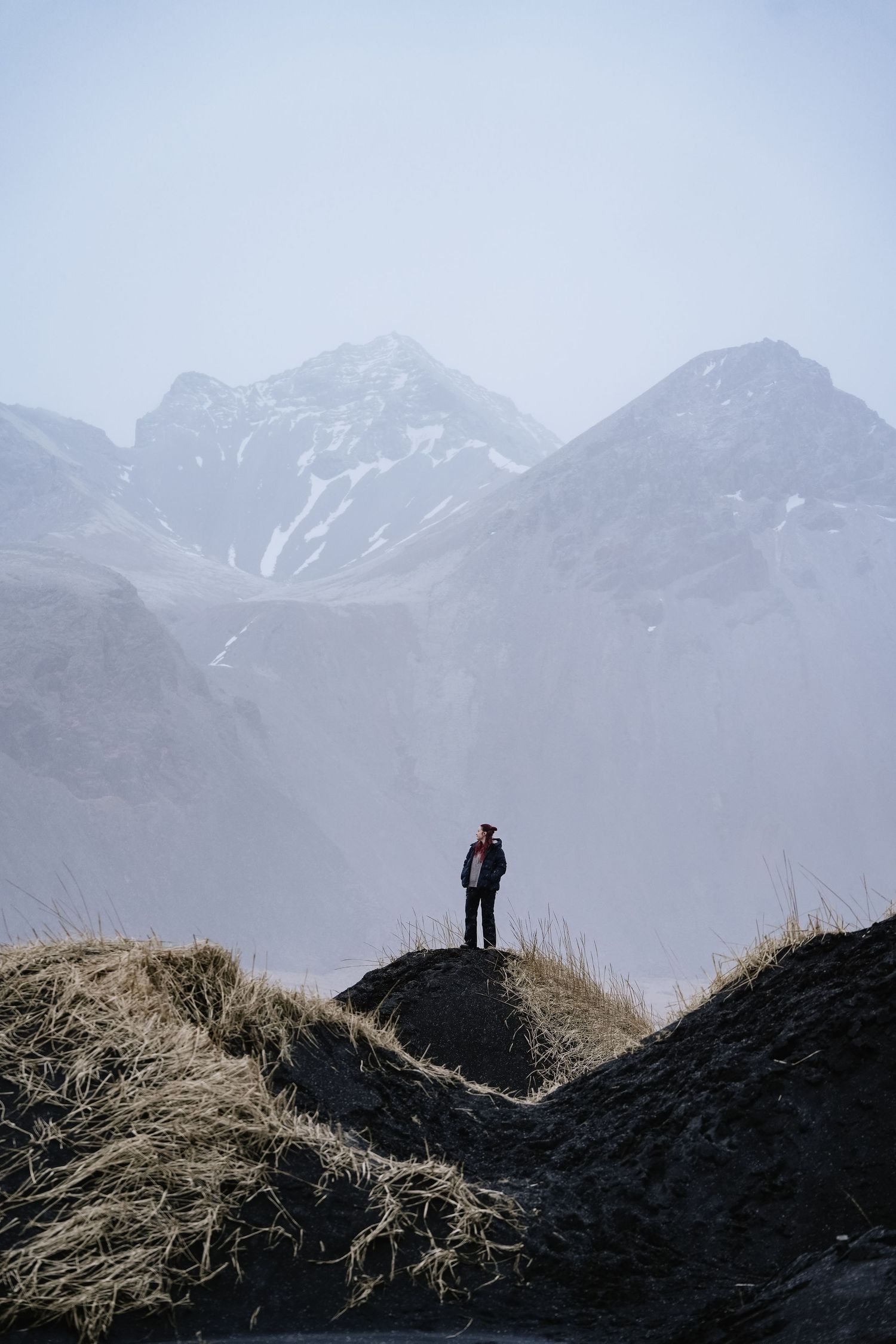 Distant figure stands atop a hill silhouetted against snow-capped mountain peaks. Iceland.