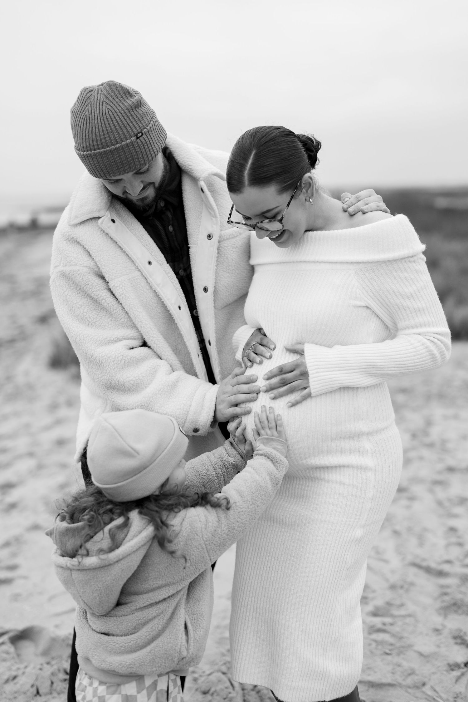 A couple embraces tenderly in matching white sweaters during a winter photoshoot. Earlhams Beach, Harwich, Essex.