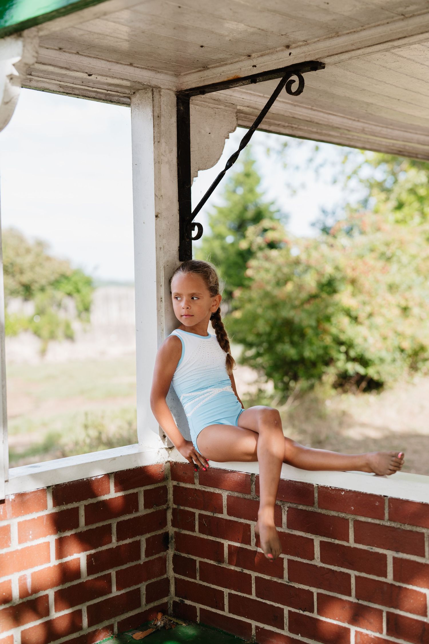 Student practicing gymnastics poses on brick ledge of covered porch. Manningtree, Essex.