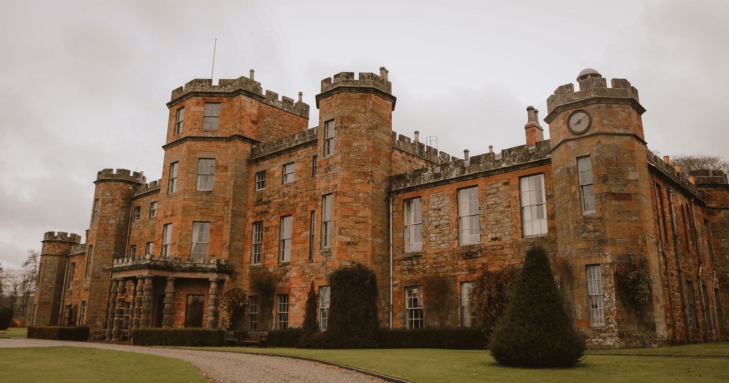 Imposing stone castle with turrets and Gothic architecture stands against cloudy sky at Cholmondeley Castle in England.