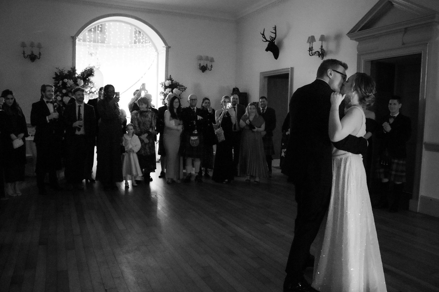 A wedding couple shares their first dance on a polished ballroom floor as guests watch from the perimeter.