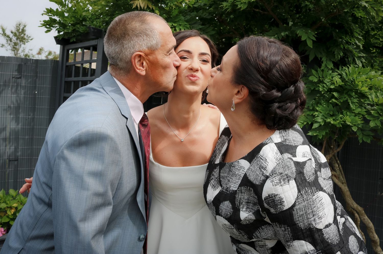 A wedding couple shares a tender kiss in a garden setting while wearing elegant gray and white attire.