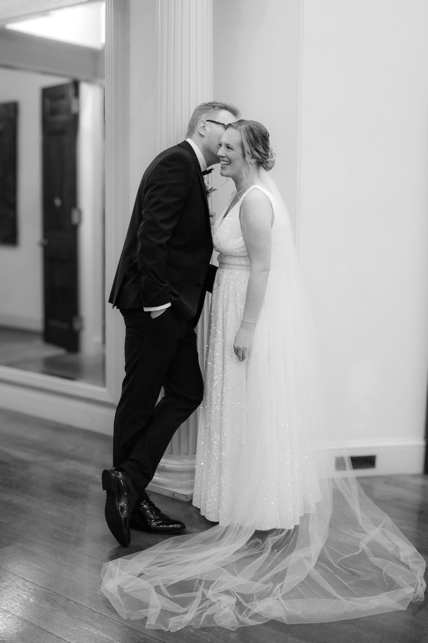Romantic black and white wedding photo with couple kissing in an elegant setting with flowing dress train.