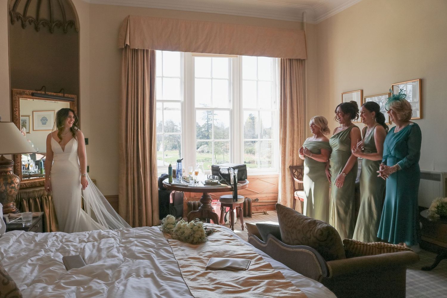 A quiet moment in a bedroom with a bride and three bridesmaids in mint-colored dresses standing beside a large window.