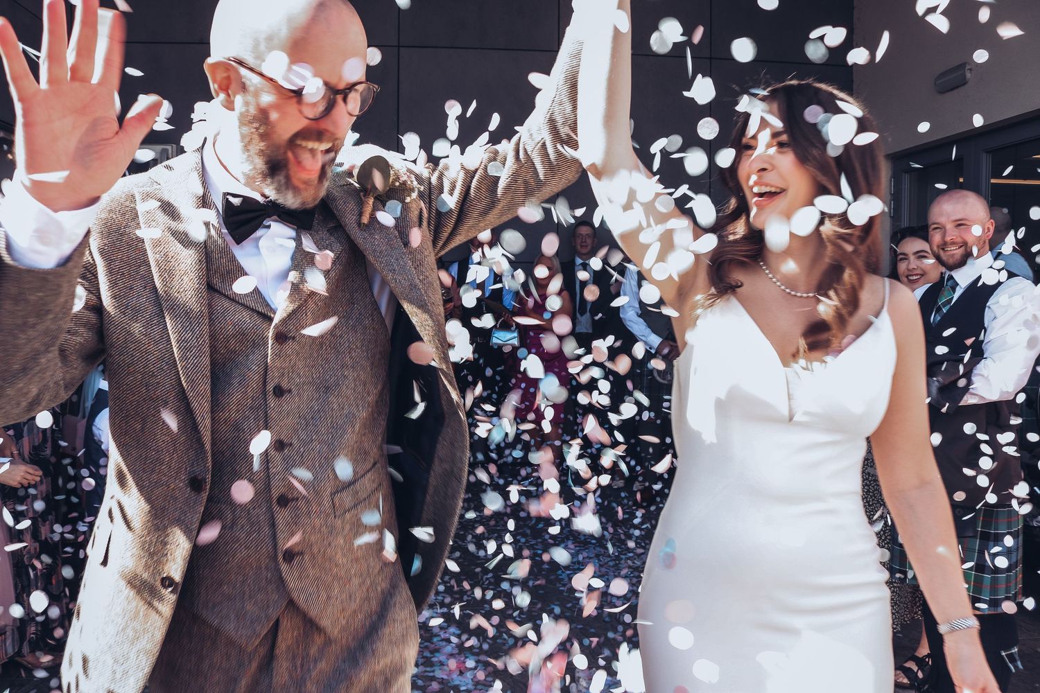 A wedding celebration with two newlyweds celebrating under falling confetti in their formal wedding attire.