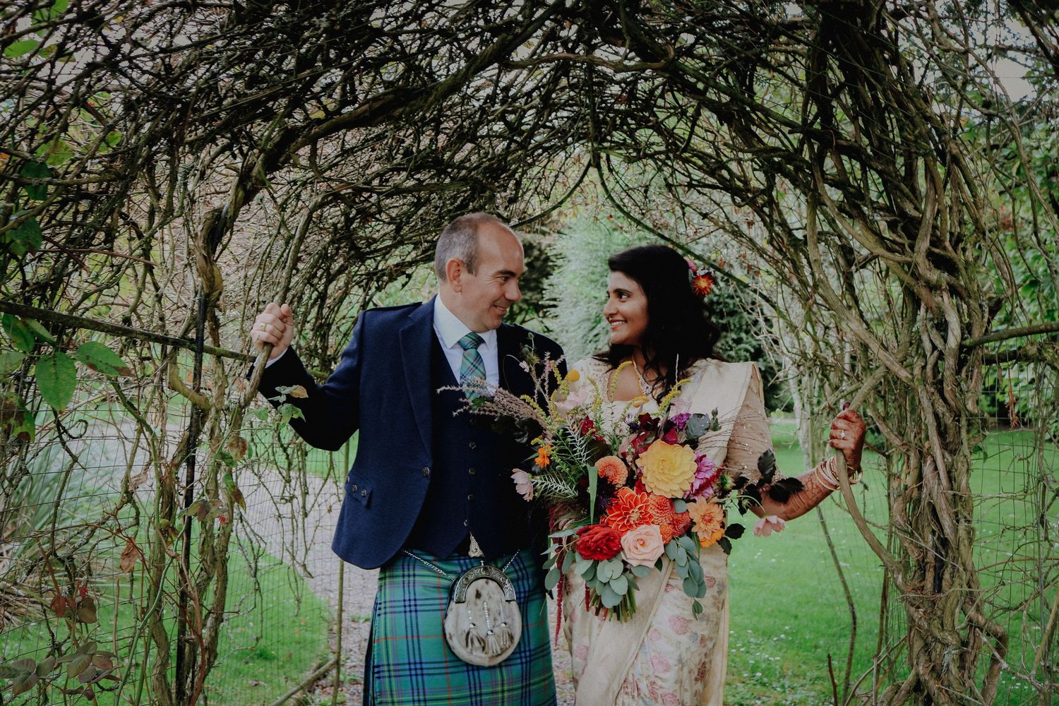 A couple joyfully shares a laugh together under a natural archway of intertwined branches during their wedding.