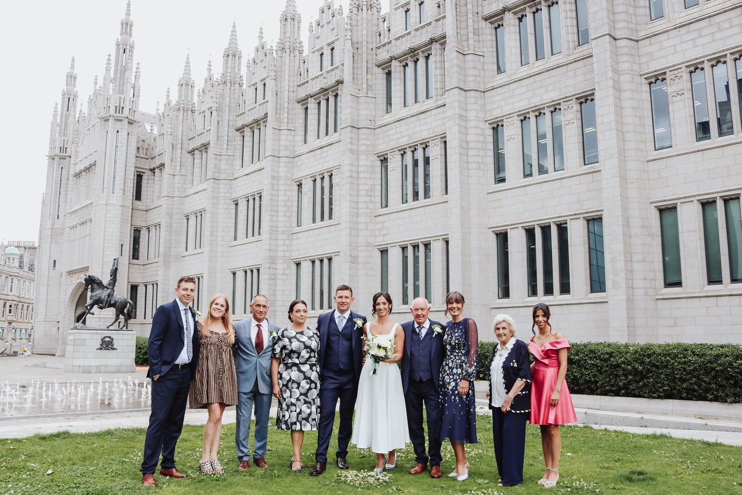 A group stands together on the lawn outside the gothic architecture of Marischal College in Aberdeen, Scotland.