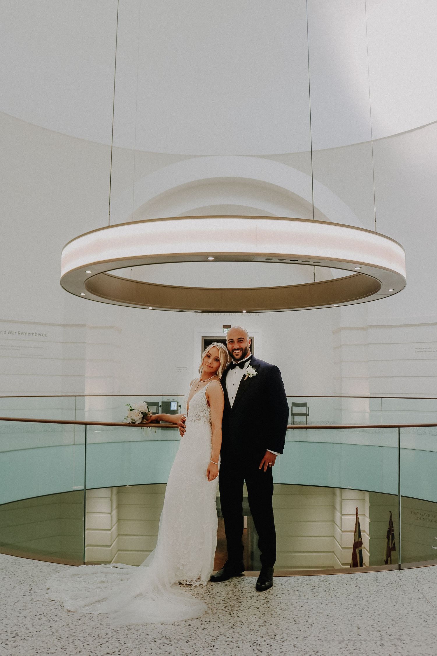 A couple stands beneath a modern circular light fixture in a minimalist white space.