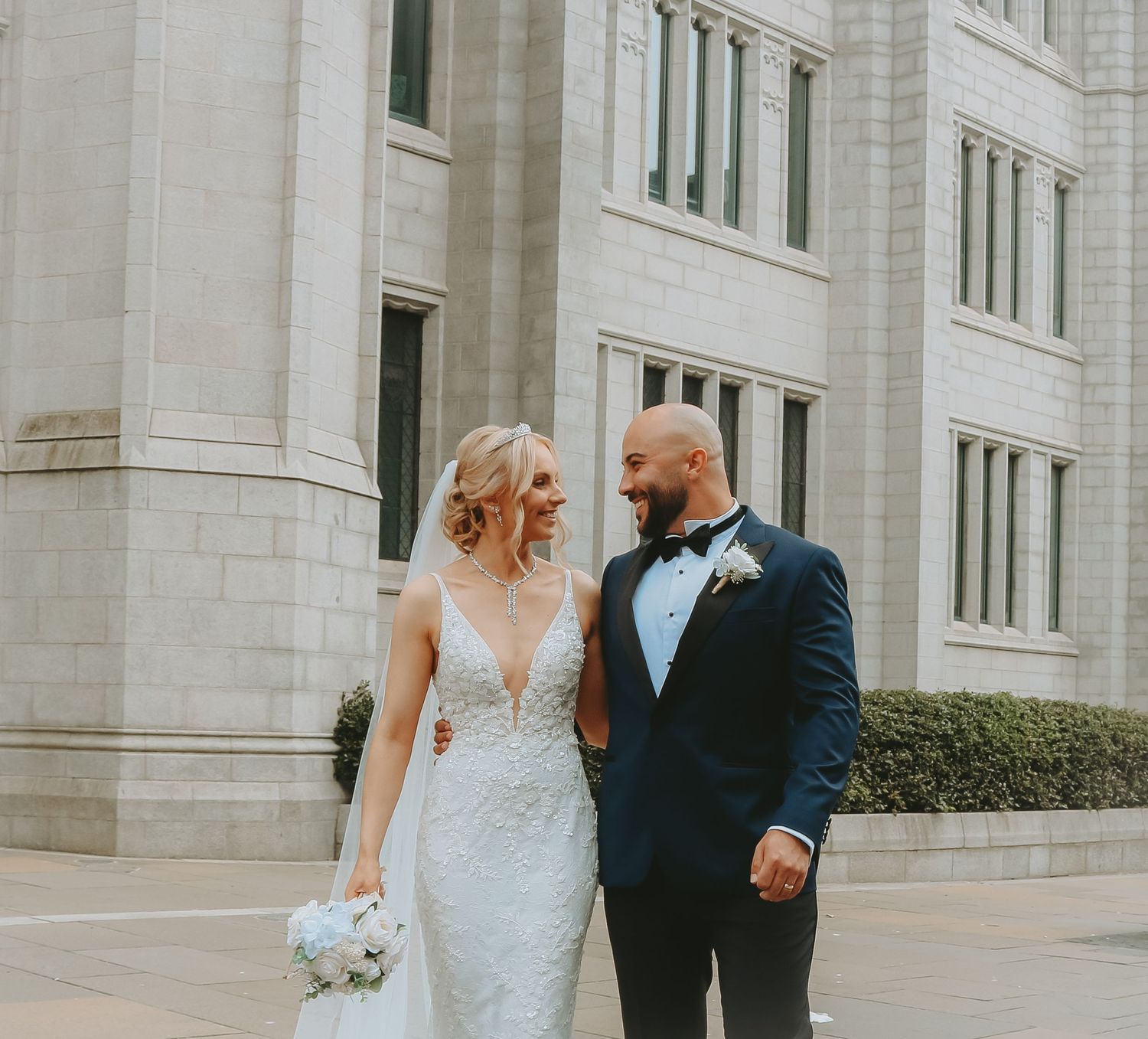 Newlywed couple poses together outside grand white stone building.