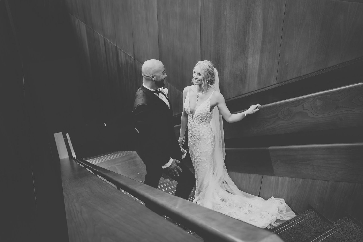 Black and white photo of couple on dramatic staircase in formal wedding attire.