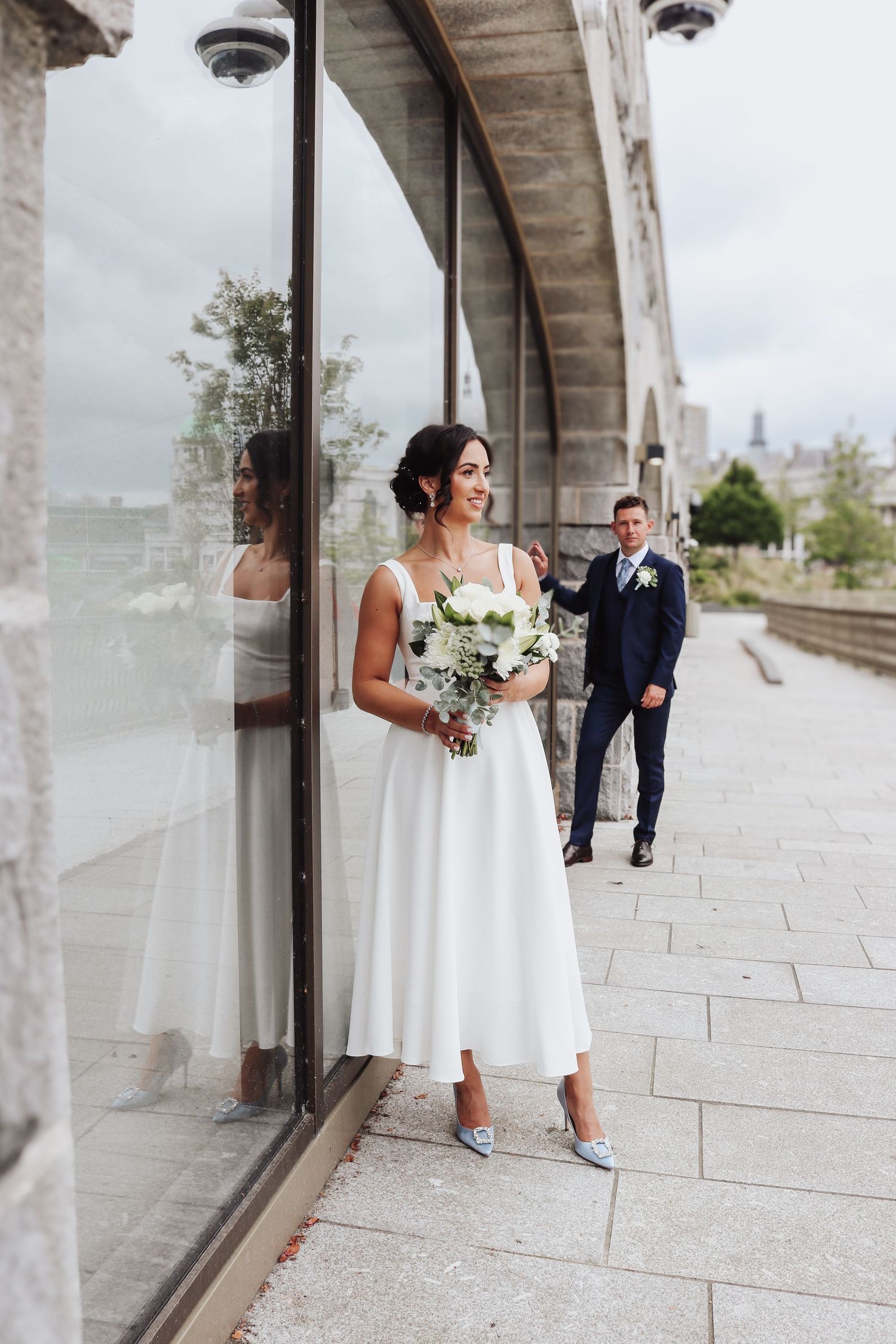 Bride and groom share romantic first look moments through reflective glass windows along a modern building exterior.