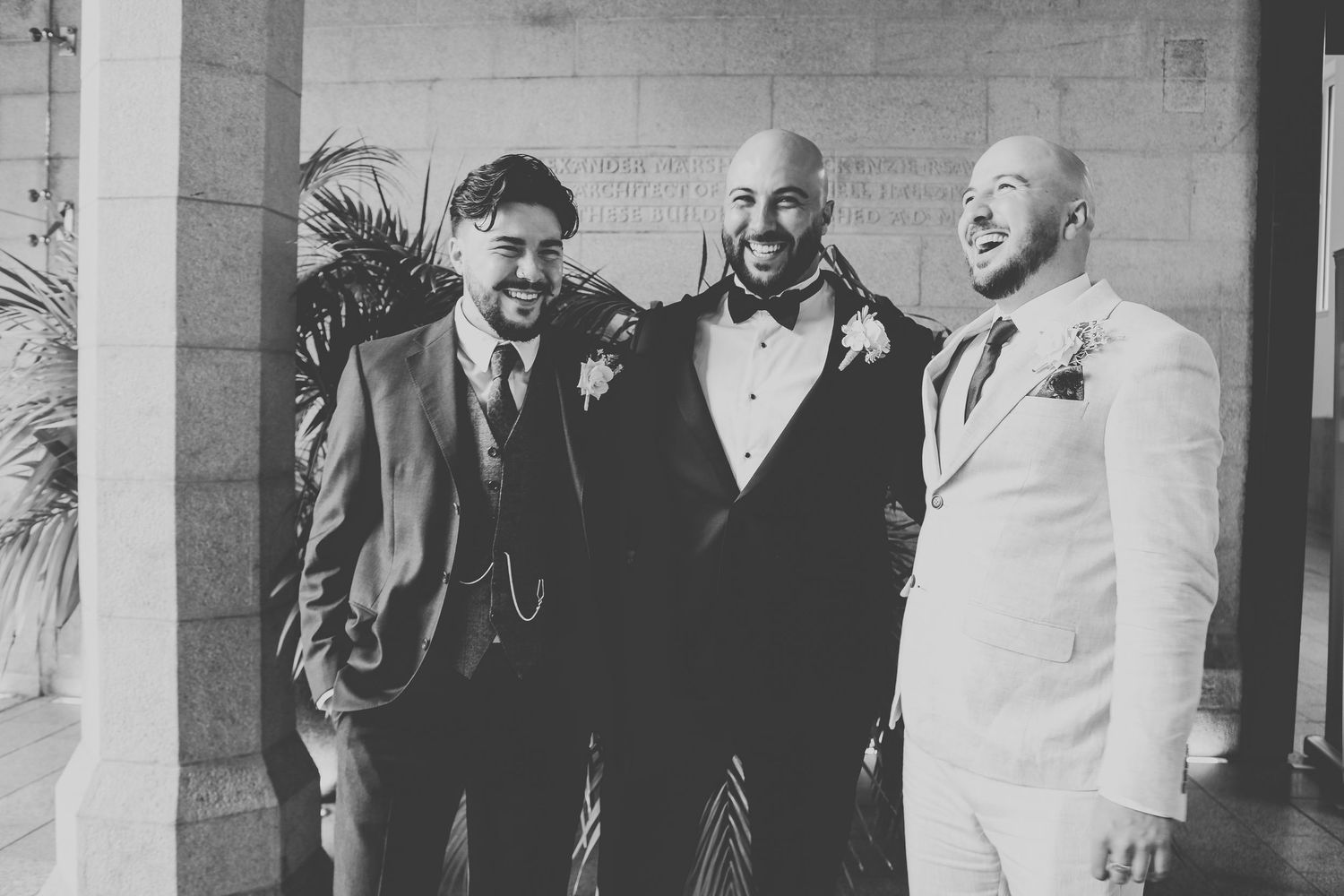 Three men in formal attire smiling and laughing together in a black and white photograph.