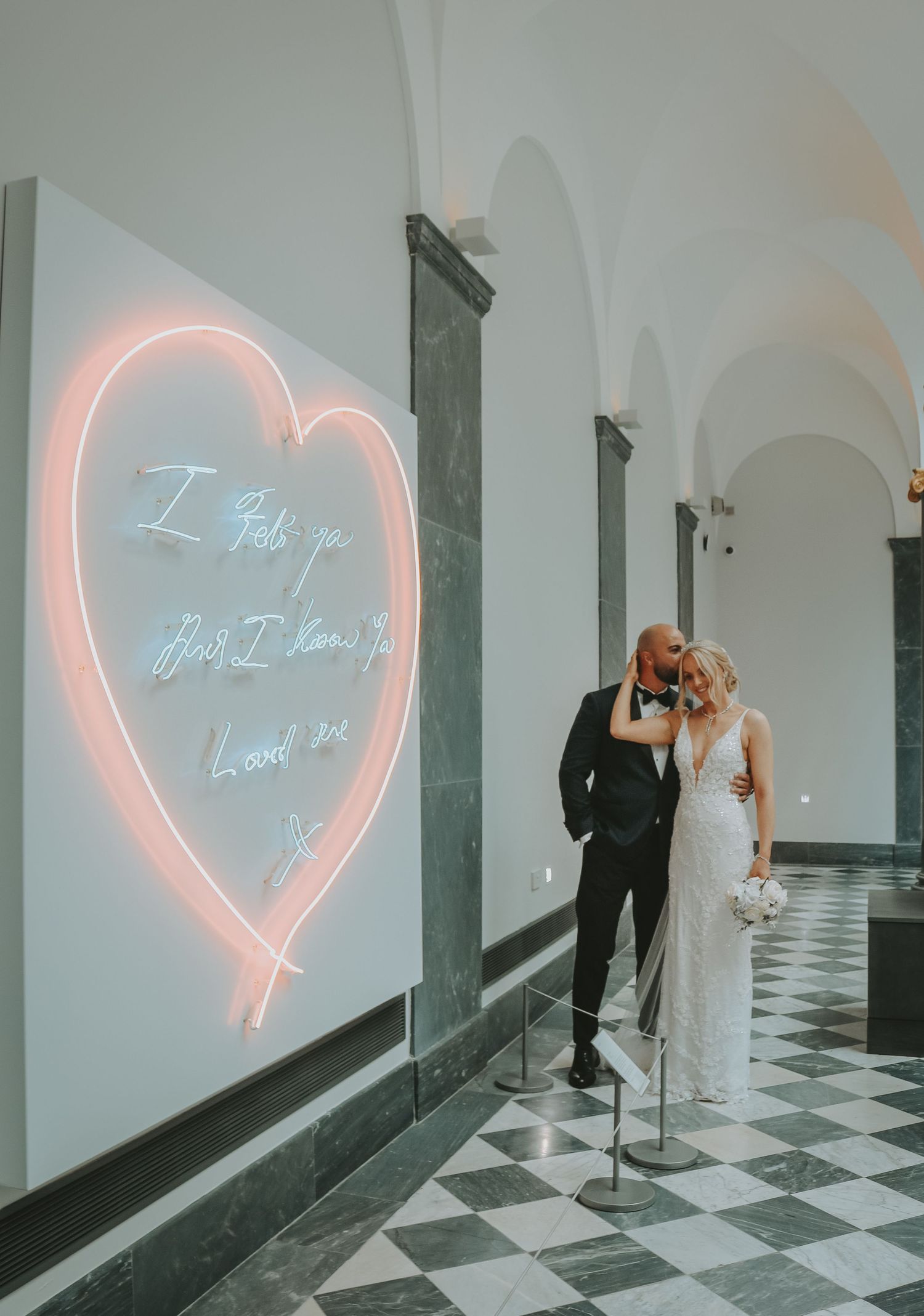 A romantic wedding scene with neon heart sign illuminating a black and white checkered hallway.