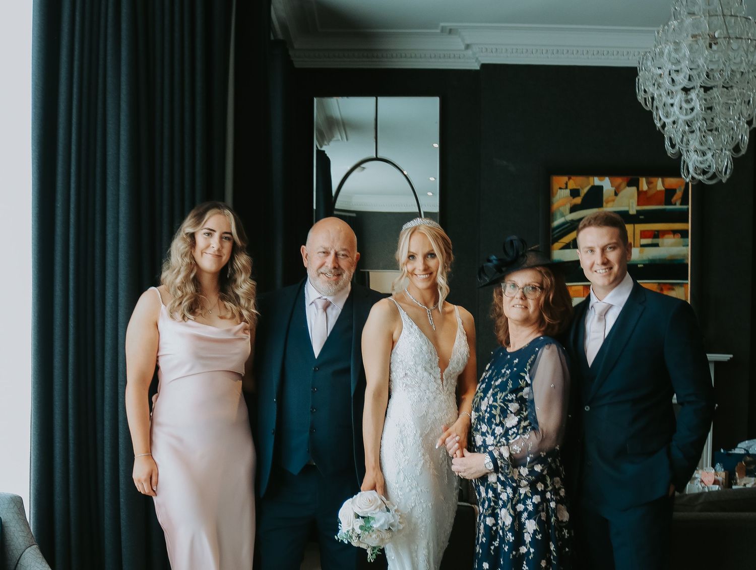 Family members gather for a formal photograph together in an elegant room with dark curtains and a crystal chandelier.
