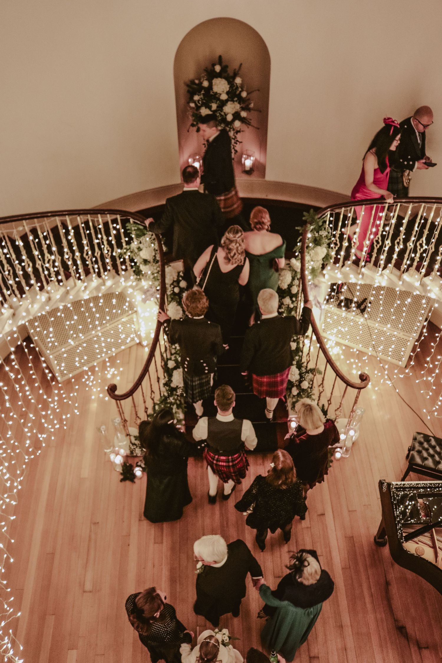 Overhead view of guests gathered on a grand staircase decorated with sparkling fairy lights and holiday decor.