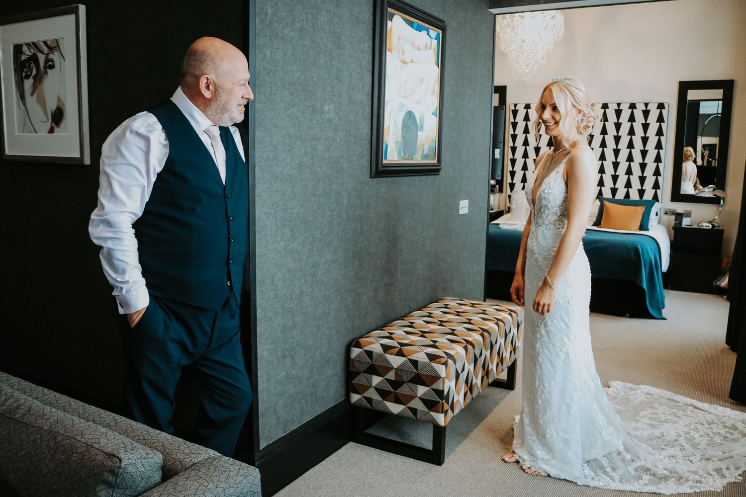 A heartfelt moment captured in a hotel room as figures interact in formal attire beside a patterned bench.