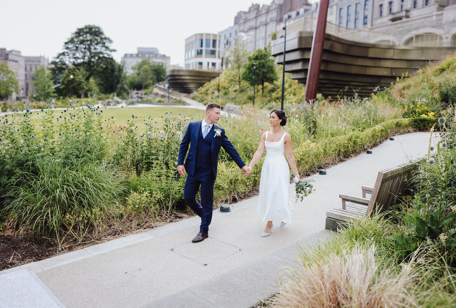 A couple walks along a winding garden path surrounded by ornamental grasses and modern architecture.