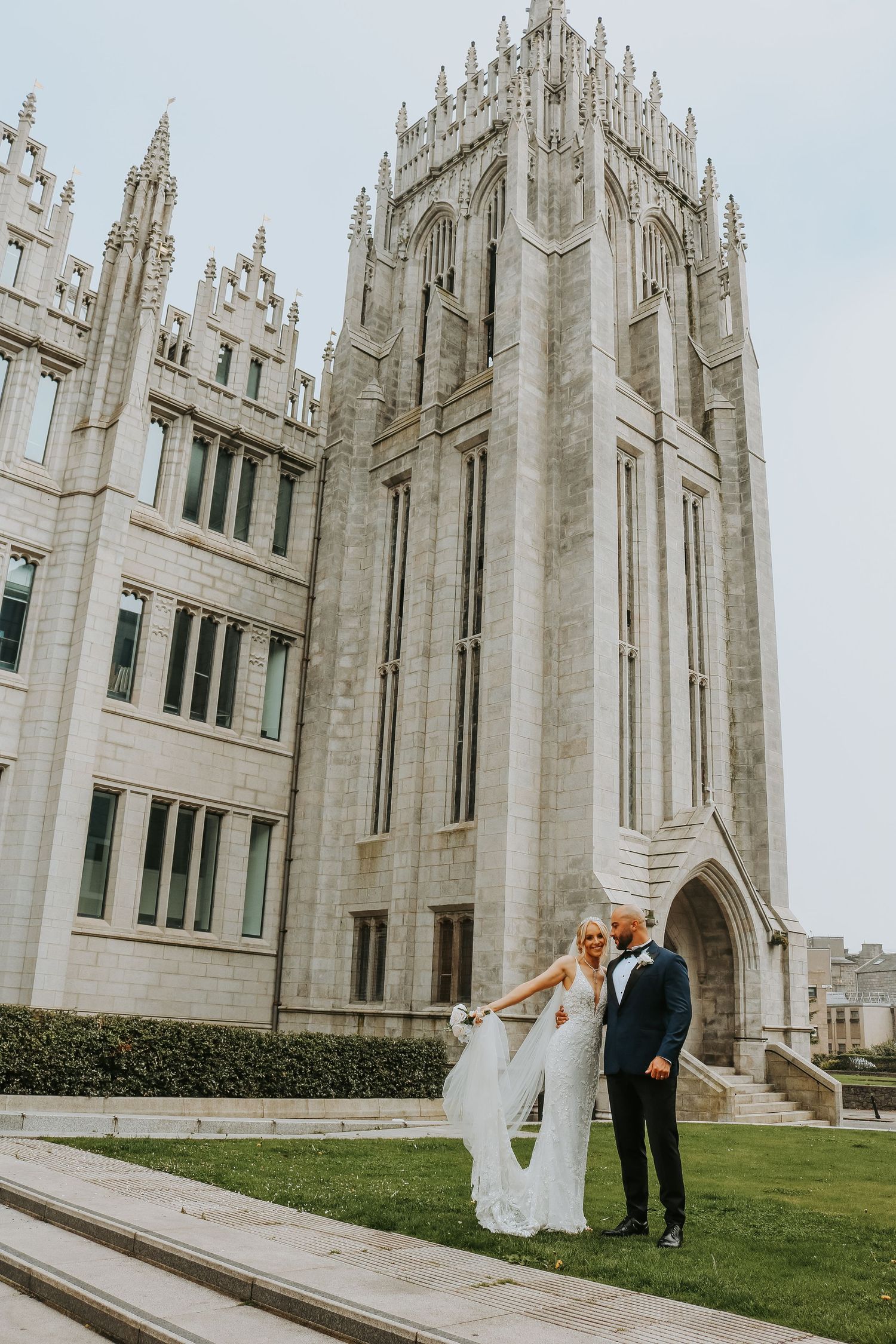 A couple poses for a wedding photo against the backdrop of a grand Gothic cathedral with ornate stone architecture.
