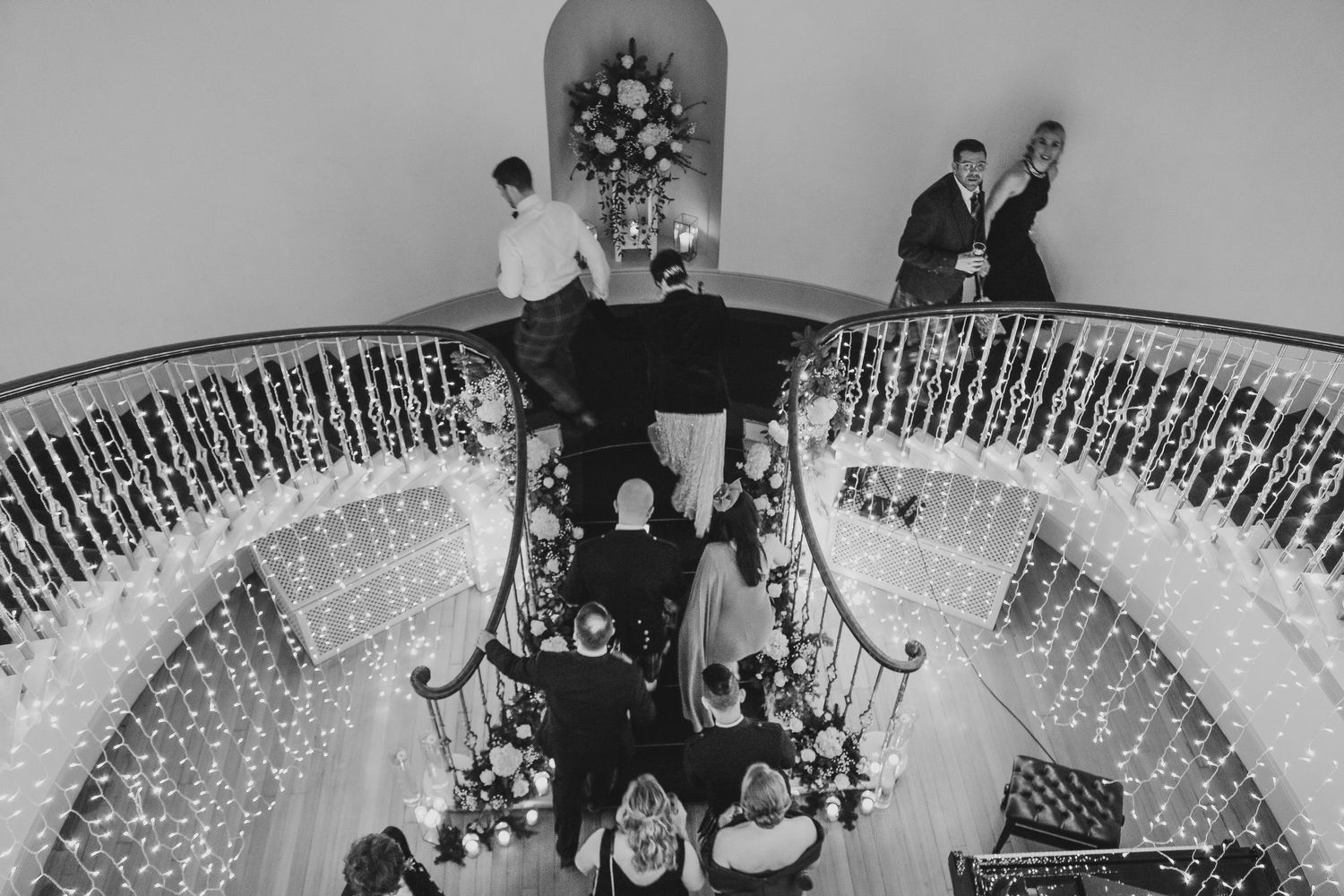 A black and white photo of an elegant curved staircase with ornate wrought iron railings and a chandelier hanging above.