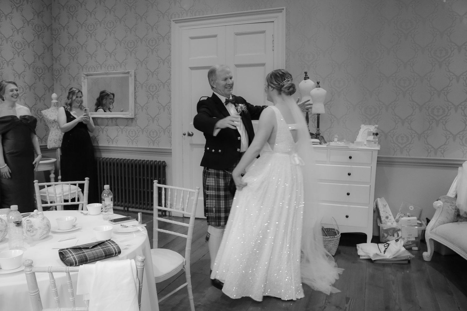 A black and white wedding photograph showing a person in a kilt dancing with someone in a flowing white wedding gown.
