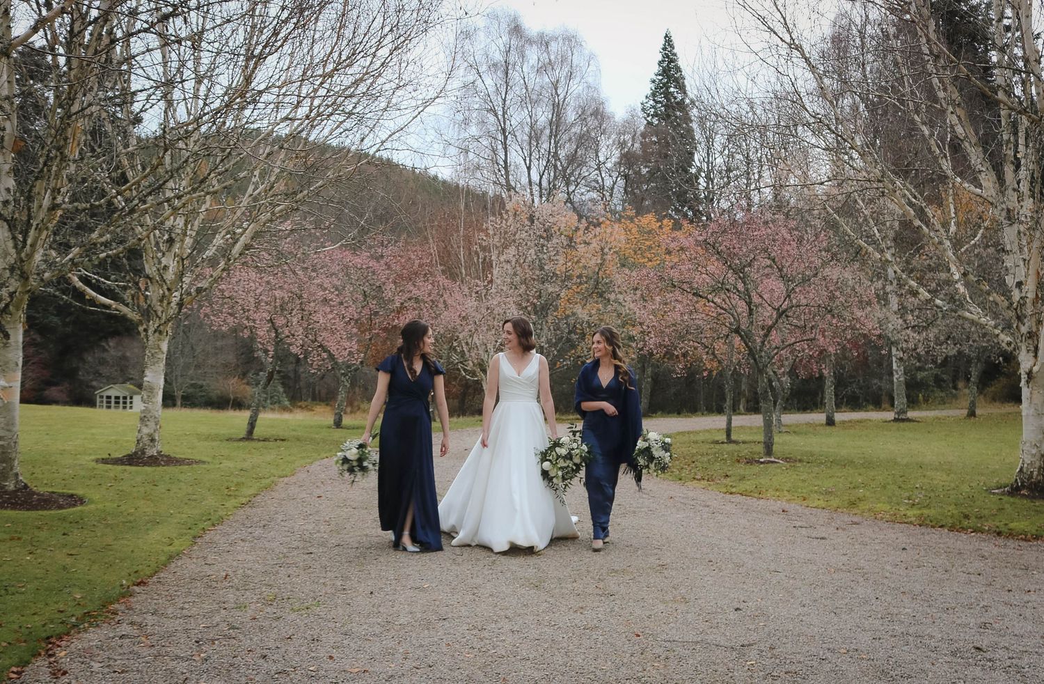 People walking down a tree-lined gravel path in a park during early spring with blooming cherry trees.