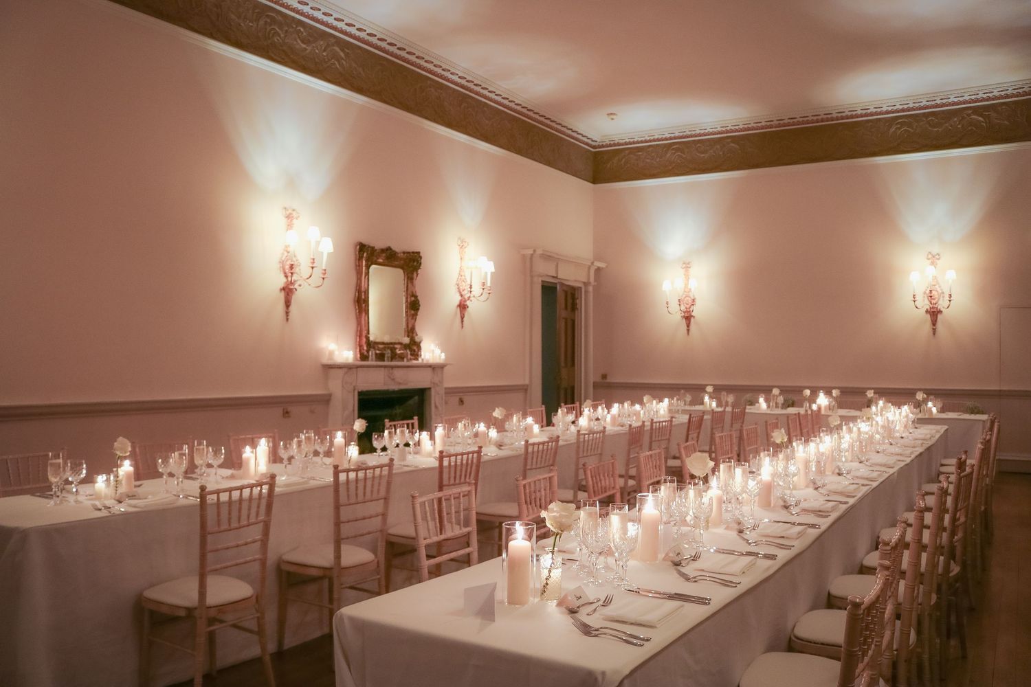 Elegant banquet table setup with white linens and glowing candles in a room with vintage wall sconces and soft lighting.