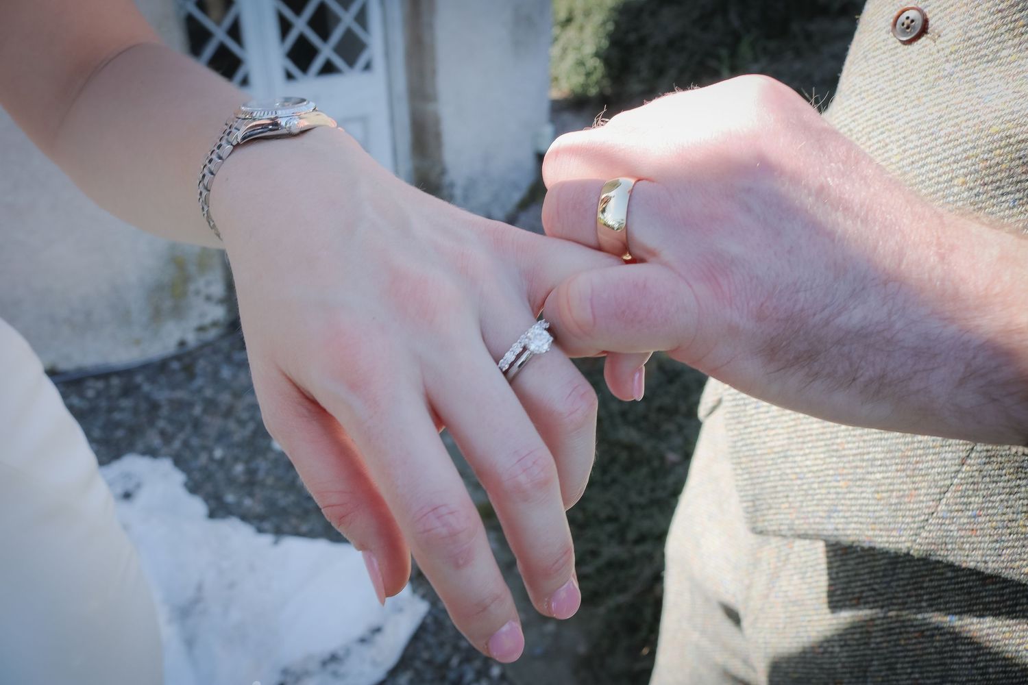 Close-up photo showing two hands wearing gold wedding bands meeting in a tender moment.