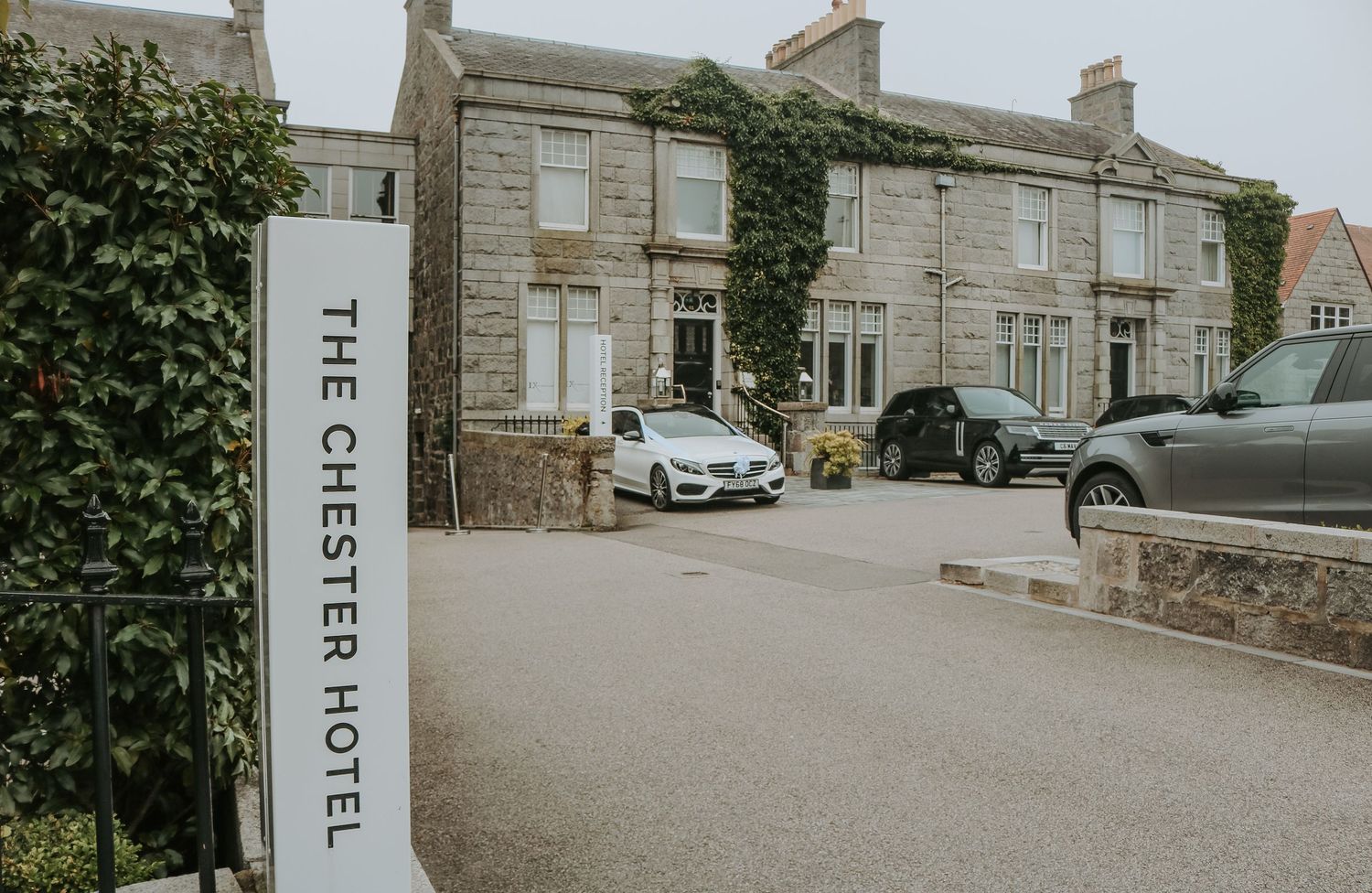 The Chester Hotel exterior with parked cars and ivy-covered stone walls along a curved driveway on an overcast day.