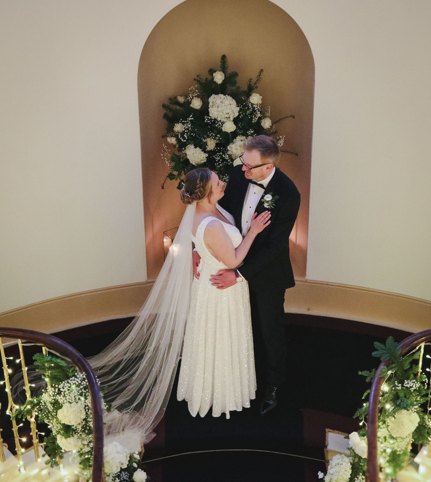A couple shares an intimate moment in front of a floral arch during their wedding ceremony at an elegant venue.