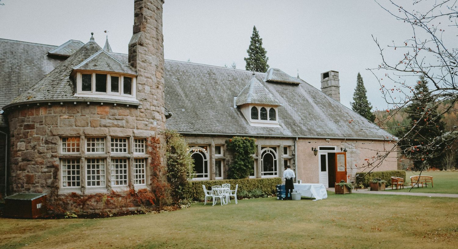 A charming stone cottage with bay windows, dormers, and ivy-covered walls sits on a landscaped lawn.