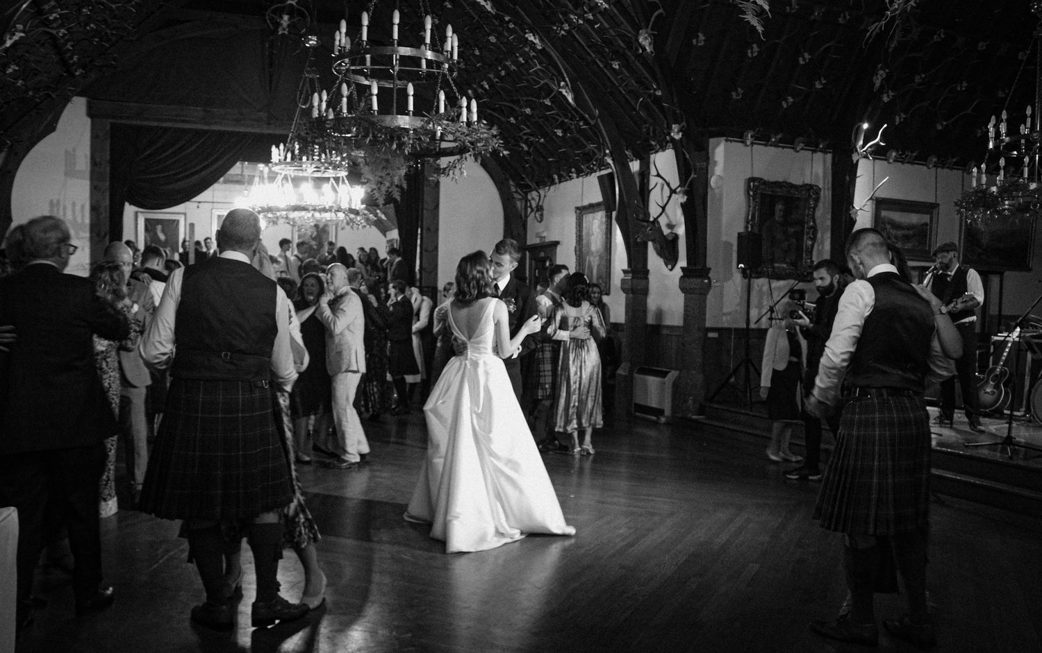 Black and white photo of wedding reception dancing in a traditional venue with chandelier and guests on the dance floor.