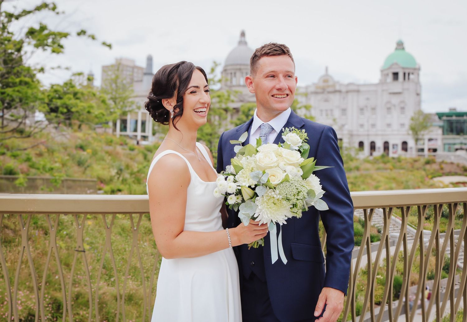 Newlyweds share joyful moments together at a scenic coastal location on their wedding day as waves crash behind them.