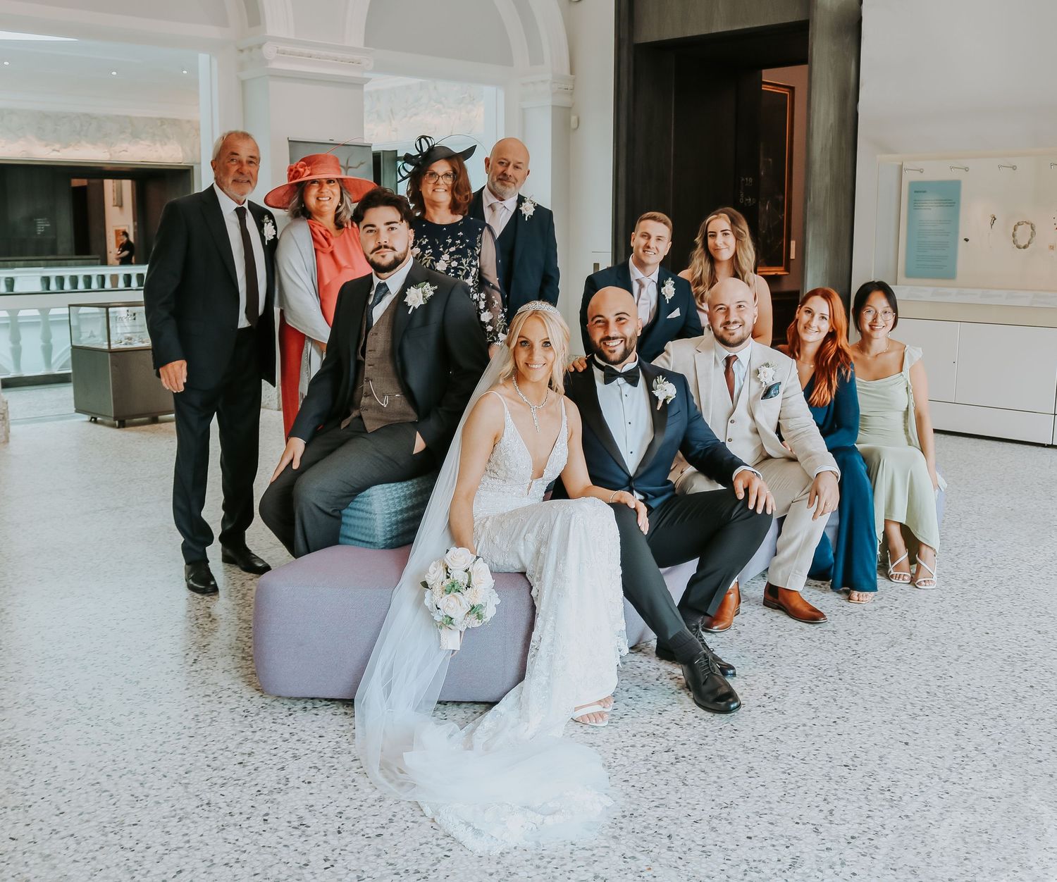 Wedding party poses together on grey lounge furniture in elegant indoor venue.