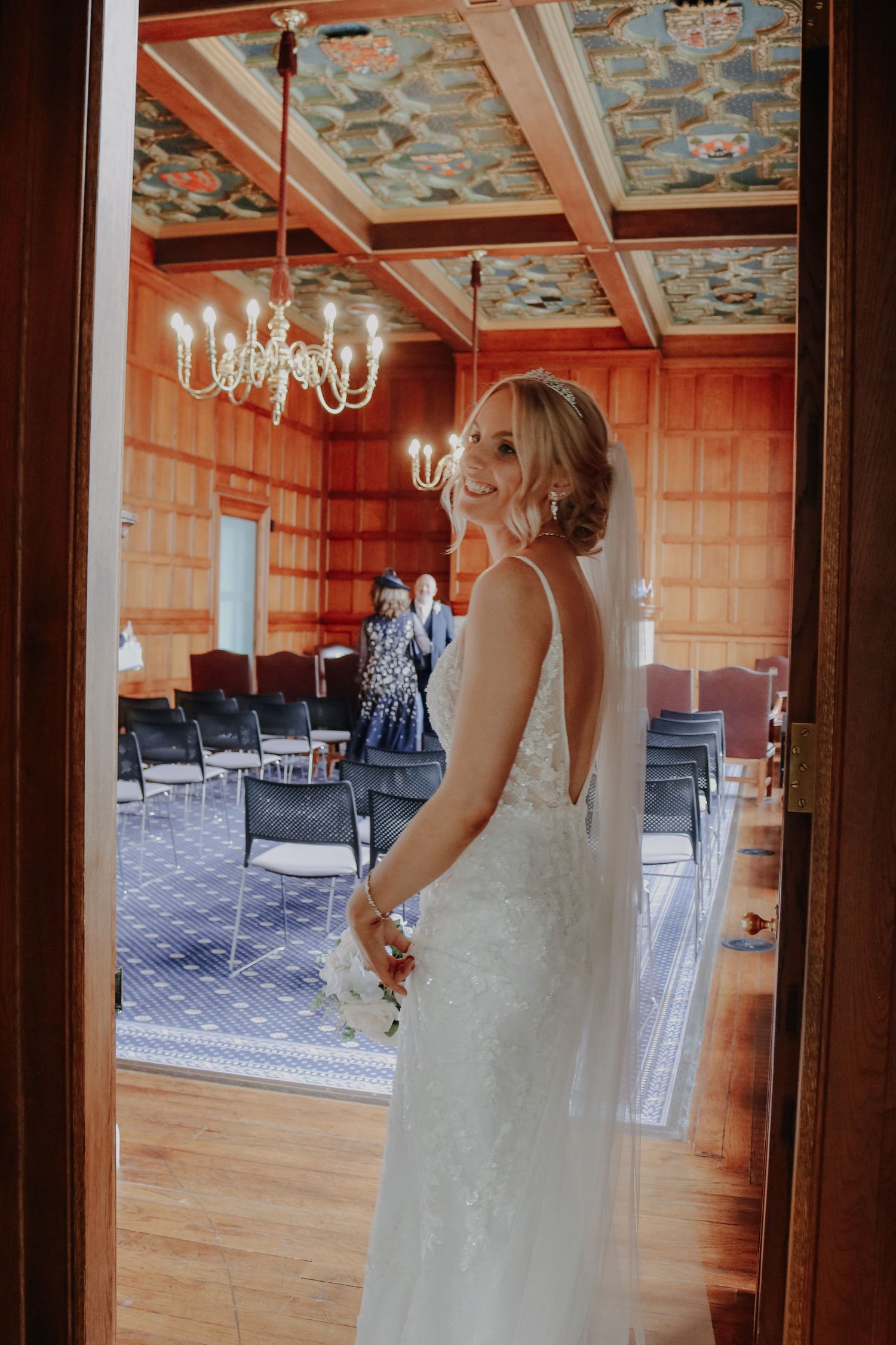 Elegant event venue with a crystal chandelier and patterned ceiling features wooden walls and rows of chairs.