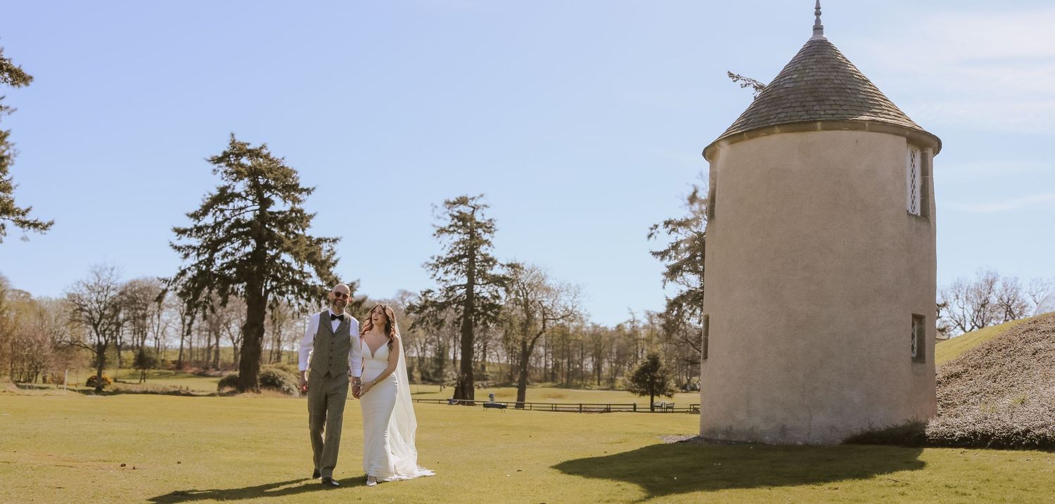 A couple poses near a historic stone tower on a sunny day at a scenic golf course.