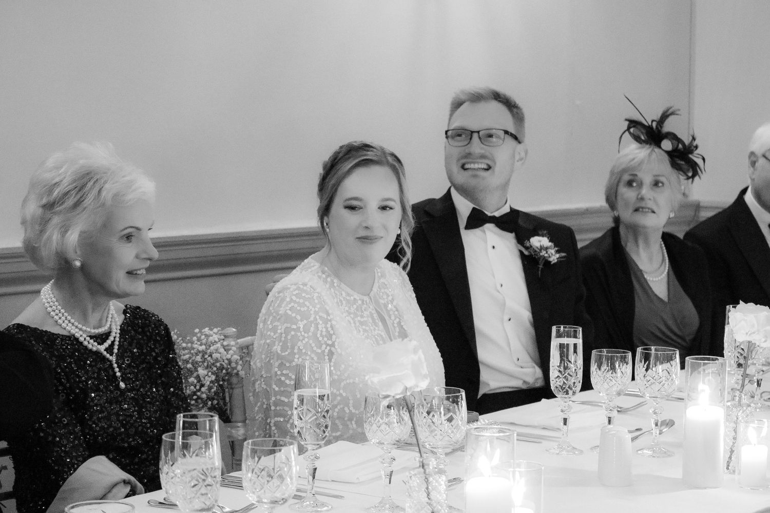 Black and white photo of guests in formal attire laughing together at an elegant reception dinner table setting.