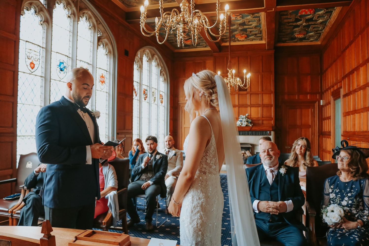 Intimate wedding ceremony taking place in an ornate wood-paneled room with Gothic windows and chandeliers.